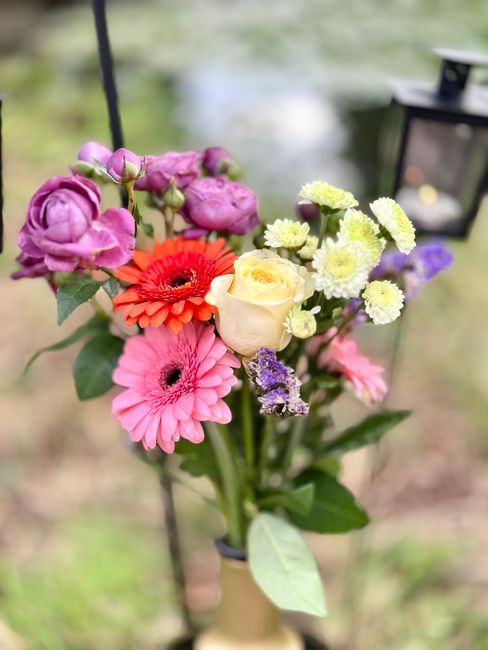 A vibrant bouquet of fresh flowers arranged in a casual, natural style, featuring pink gerbera daisies, orange gerbera, pale yellow roses, purple lisianthus, small white and yellow chrysanthemums, and