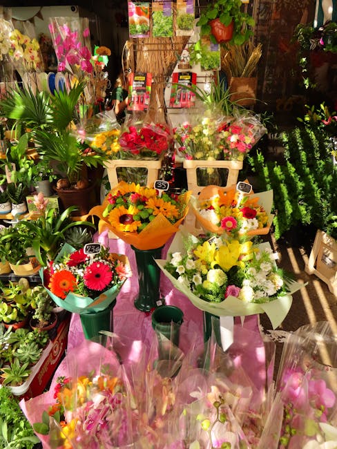 A vibrant display of fresh floral bouquets arranged on a pink table in a flower shop, featuring a variety of colorful flowers including pink, yellow, orange, and white blooms. The bouquets are wrapped